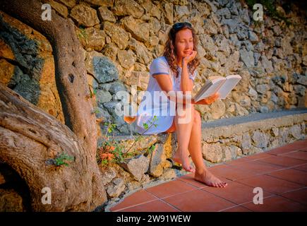 Woman reading book near stone wall Stock Photo