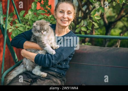 Smiling woman sitting with cat on swing in garden Stock Photo
