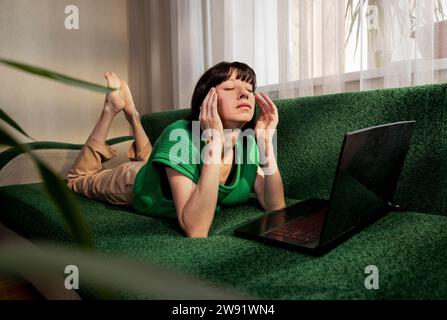 Depressed freelancer lying on sofa with laptop at home Stock Photo
