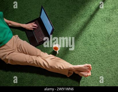 Freelancer with cup of tea using laptop on carpet at home Stock Photo