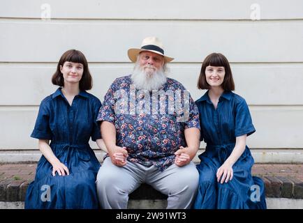 Father holding hands with daughters sitting in front of wall Stock Photo