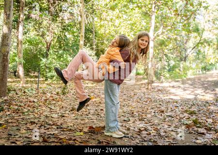 Smiling girl giving piggyback ride to friend in park Stock Photo