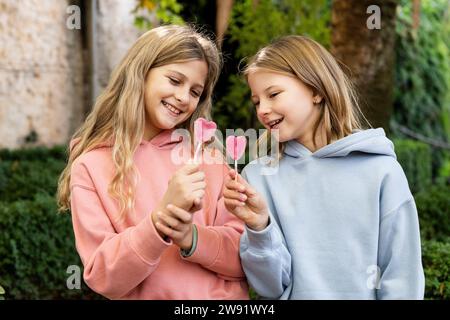 Happy girls holding heart shaped lollipop candies in park Stock Photo