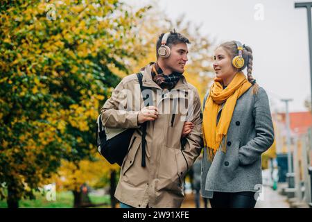 Young couple with wireless headphones walking at street Stock Photo