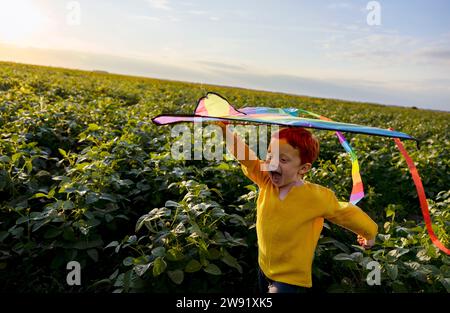 Happy boy holding kite on head and running in agricultural field Stock Photo