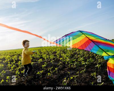Smiling boy flying kite in agricultural field under sky Stock Photo