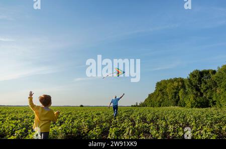 Grandfather and grandson flying kite in agricultural field under sky Stock Photo