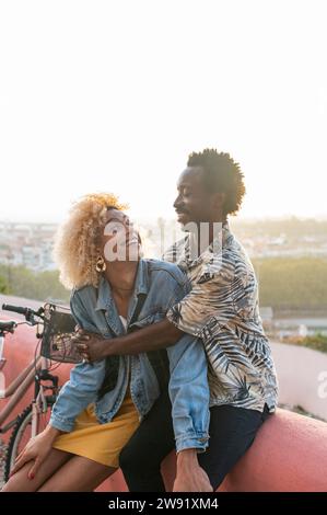 Smiling boyfriend embracing transgender woman sitting on wall Stock Photo