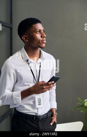 Thoughtful young businessman holding smart phone in office Stock Photo