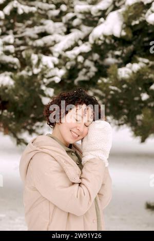 Smiling woman wearing gloves and rubbing hands in winter forest Stock Photo