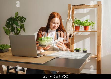 Smiling botanist using smart phone with laptop on desk at home office Stock Photo