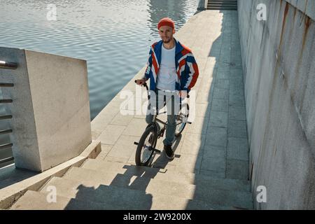 Smiling man standing with BMX bike near lake on embankment Stock Photo