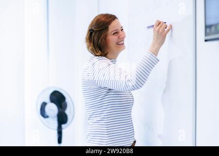 Happy teacher writing on whiteboard and teaching in classroom Stock Photo