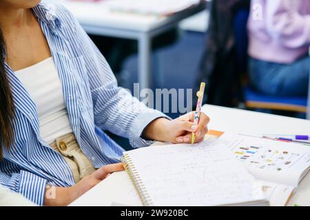 Student writing in notebook at desk in classroom Stock Photo