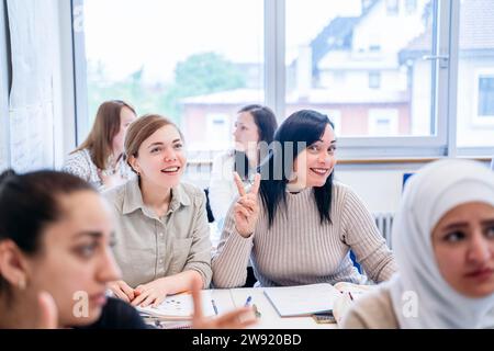 Smiling student gesturing peace sign sitting by friend in classroom Stock Photo