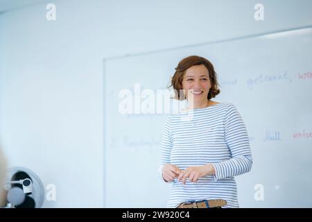 Smiling teacher standing in front of whiteboard at classroom Stock Photo