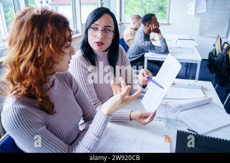 Multi-ethnic students discussing over notes at desk in classroom Stock Photo