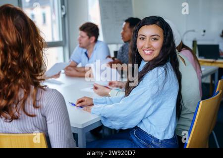 Smiling student sitting with multi-ethnic friends at desk in classroom Stock Photo