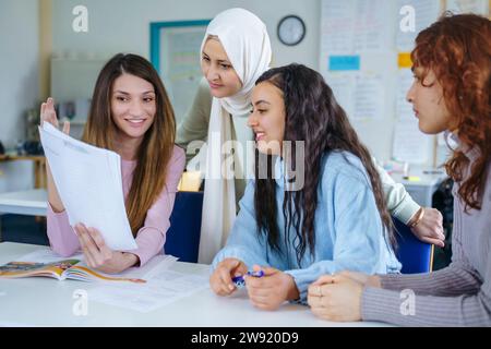 Smiling multi-ethnic students discussing over paper at desk in classroom Stock Photo