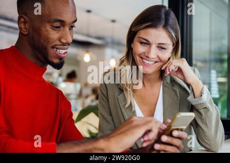 Smiling businesswoman sitting with colleague using smart phone at cafe Stock Photo
