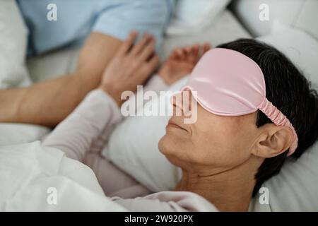 Woman wearing sleeping mask while lying in bed next to her husband Stock Photo