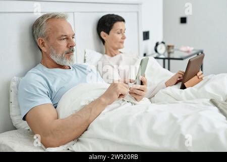 Man using smartphone while his wife lying next to him in bed with digital tablet in the morning Stock Photo