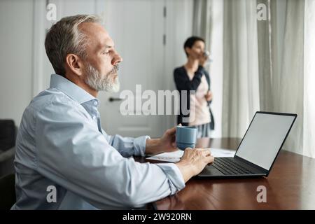 Man using laptop and drinking tea while spending time at home with wife Stock Photo