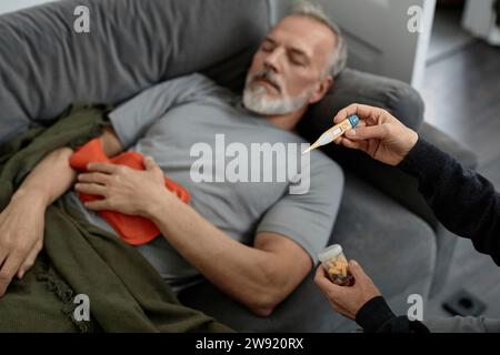 Unrecognizable woman looking at thermometer while sitting next to sick husband at home Stock Photo