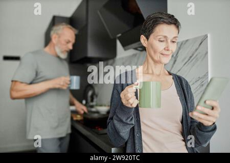 Woman using smartphone while her husband is cooking lunch in background Stock Photo