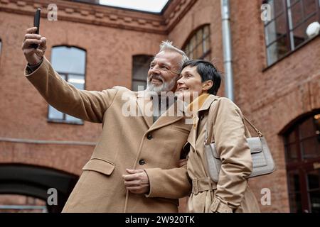 Happy elderly couple taking selfie on smartphone during city walk Stock Photo