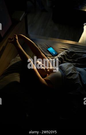 Young woman stretching arms and waking up in bed at home Stock Photo