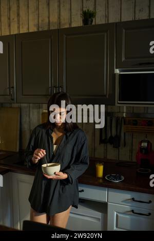 Woman holding bowl and having breakfast in kitchen at home Stock Photo