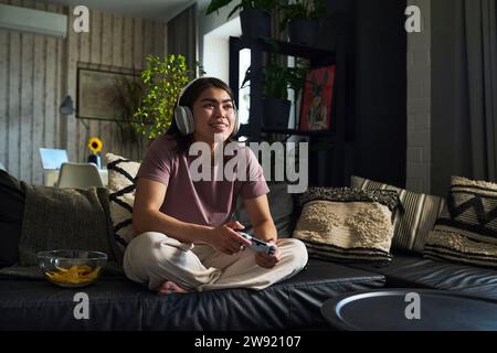 Happy young woman playing video game with controller on sofa at home Stock Photo