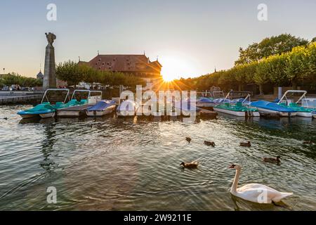 Germany, Baden-Wurttemberg, Konstanz, Swans swimming in harbor on shore of Bodensee at sunset Stock Photo