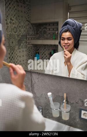 Young woman brushing teeth and looking in mirror at home Stock Photo