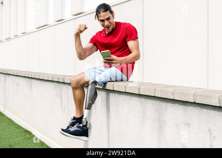 Happy man with disability flexing muscles and using smart phone Stock Photo
