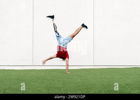 Young man with prosthetic leg doing handstand in front of wall Stock Photo