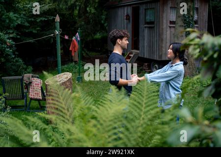 Smiling man holding hands with woman in front of wooden cabin Stock Photo