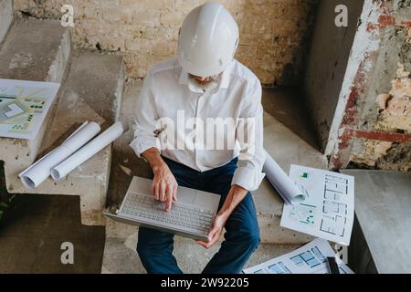Architect using laptop with blueprints on staircase at site Stock Photo