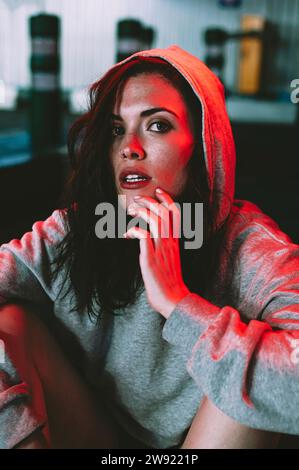 Woman wearing hooded shirt sitting under neon lights Stock Photo