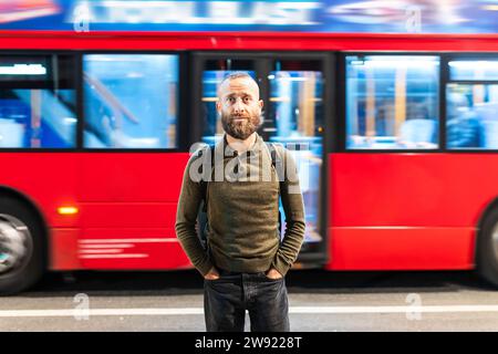 Man with hands in pockets standing in front of moving bus in city Stock Photo