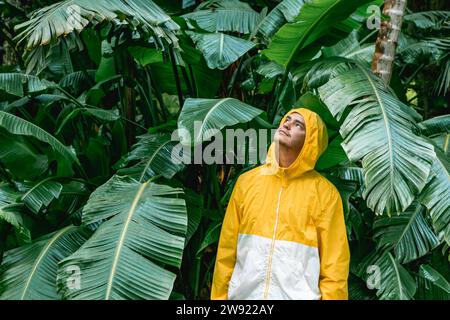 Young man wearing raincoat and standing in front of trees Stock Photo