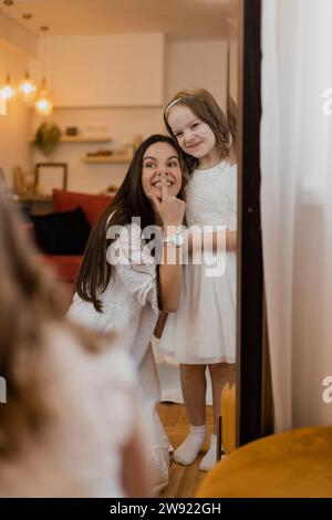 Playful mother touching nose with daughter making face in mirror at home Stock Photo