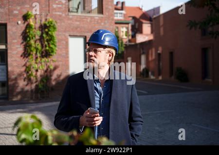 Mature architect holding smart phone standing in front of buildings Stock Photo