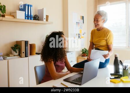 Smiling businesswoman talking to colleague with laptop on table in office Stock Photo