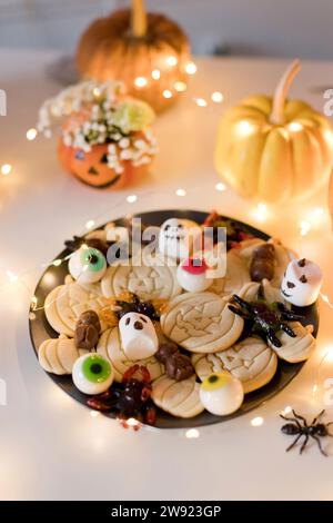 Plate of cookies with artificial spider near pumpkins and string light on table Stock Photo