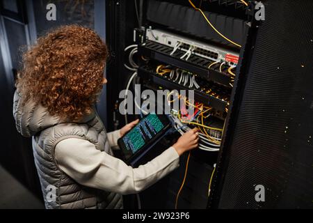 IT professional using tablet PC with data on screen and connecting cables in server room Stock Photo