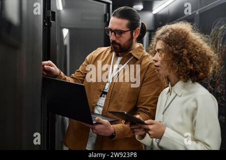 IT professionals examining servers with laptop and tablet PC in data center Stock Photo