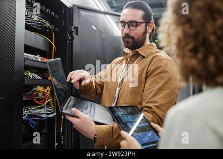 IT professionals discussing over data on laptop and tablet PC in server room Stock Photo