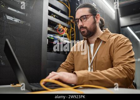 Engineer wearing eyeglasses and typing on laptop in data center Stock Photo